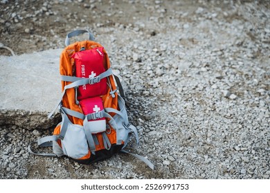 A durable and sturdy backpack, equipped with a comprehensive first aid kit, rests against the ground, clearly visible for anyone passing by in case of emergencies or for outdoor adventure activities