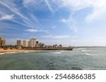 Durban beachfront, a popular holiday destination with high rise apartments and hotels on the foreshore and piers jutting out to sea, and a blue sky with clouds in the city of Durban in South Africa.