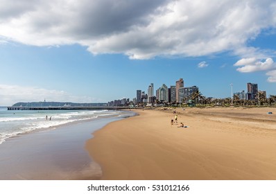 DURBAN, SOUTH AFRICA - DECEMBER 2, 2016: Many unknown  early morning beach goers and  calm sea against blue cloudy sky and golden mile city skyline in Durban