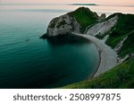 Durdle Door, Dorset, England is a stunning natural rock arch that stretches into the sea, created when waves eroded through the limestone cliffs around 10,000 years ago. 