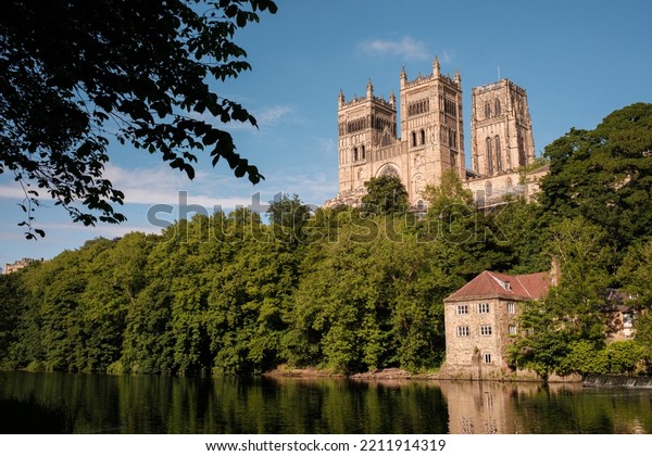 Durham\
England: 2022-06-07: Durham Cathedral exterior during sunny summer\
day. View from river wear with lush green\
trees