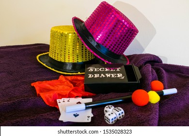 Durham, UK - 18 October 2019: Magic Show Magicians Trick Concept Background. Children's Magic Box With Sequined Top Hats, Magic Wand, Playing Cards, Cup And Ball Trick, Secret Drawer Box And Die.