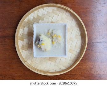 Durian sticky rice in coconut milk or serawa durian dan pulut kukus. Malaysia local dessert. Milky and creamy coconut milk or santan. Added some corn kernel. White and square ceramic bowl. Bamboo tray