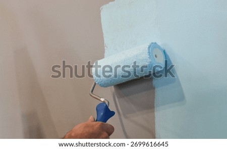During the apartment remodeling process, a worker uses a paint roller to cover the wall surface with white color, transforming the living space with new paint.