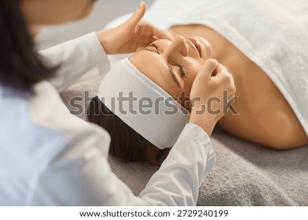 During a calm spa session, a professional esthetician does a gentle facial massage for a beautiful young woman, with cleansing and skincare treatment to support wellness and beauty