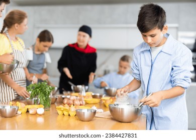 During culinary classes, teen boy combine essential components in mixing bowl and readies dough for bread rolls. In background, blurry children stand near kitchen table and listen to chef explanations - Powered by Shutterstock