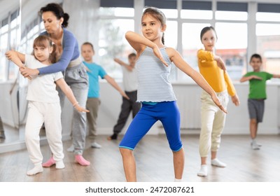 During dance workshop, girl with team of young like-minded children learn to dance modern dances. Woman teacher corrects movements of hands and body, instructs students to perform dance movements - Powered by Shutterstock