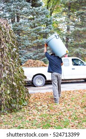 During Fall Clean Up A Man Carries A Trash Can Full Of Leaves To Dump Into The Back Of A Waiting Pickup Truck