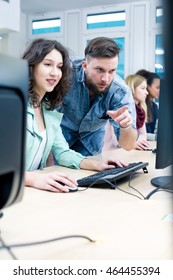 During IT lessons teacher points something to female student on a computer screen
