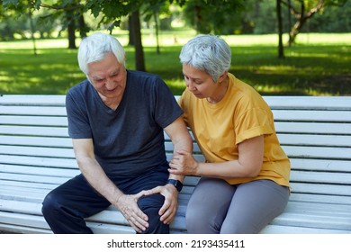 During morning sportive stroll or making exercises in a park, elderly 60s man got injured his knee, gripping leg sit in bench with caring disappointed wife. Traumas, injures of older people concept - Powered by Shutterstock