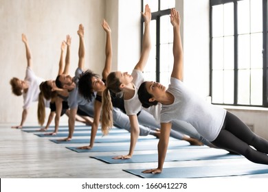 During morning yoga session lead by Indian ethnicity female coach group of multi-ethnic seven young people performing Side Plank Pose or Vasisthasana increase stability for shoulders, hips, and spine - Powered by Shutterstock