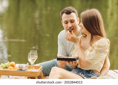 During picnic in nature, young woman feeds her man sweets from gift box . Sweet life. Happiness and serenity. Beautiful moments of life. Super day. Romantic relationships. Tenderness and care. - Powered by Shutterstock