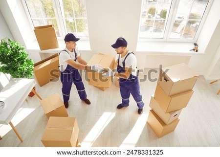 During relocation or delivery, two movers are seen carrying boxes into either a home or office space. Coordinated efforts reflect the professionalism of a relocation service.