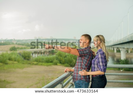 during romantic stroll guy shows girl finger into the distance. loving couple looking far ahead. make plans for future. girl in plaid shirt and shorts. Man in pants and plaid shirt. cloudy summer day