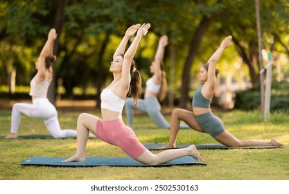 During street workout, yoga practice on lawn in public park, group of girls work with their bodies and do carry out warrior pose exercise. Girls attend outdoor yoga lesson in park. - Powered by Shutterstock