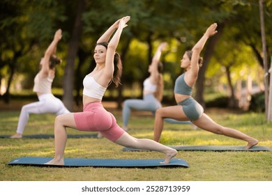 During street workout, yoga practice on lawn in public park, group of girls work with their bodies and do carry out warrior pose exercise. Girls attend outdoor yoga lesson in park. - Powered by Shutterstock