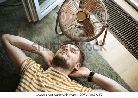During a summer heat wave, a man finds respite by lying on the floor  with the help of an electric fan. A man beats the summer heat wave by finding relief with an electric fan