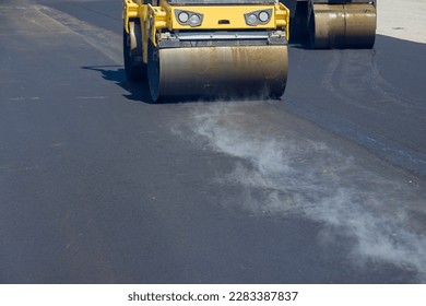 During vibratory road roller compactor process construction worker is operating machine that lays new asphalt on road - Powered by Shutterstock