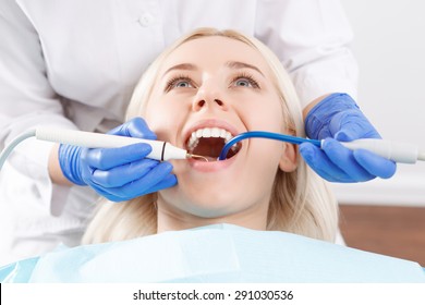 Während der Arbeit. Zahnarzt mit blauen Gummihandschuhen, die junge blonde Frau mit speziellen Geräten behandeln. 