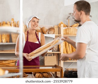 During working day, man visited bakery, communicates with female seller, makes order, buy baguettes, asks for bread products. Young female employee of bakery serves visitor - Powered by Shutterstock