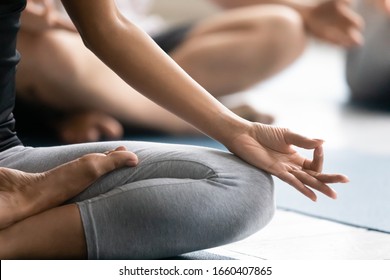 During yoga session group of people seated cross-legged improve self-awareness, increase clarity of mind, close up focus on female folded fingers Gyan mudra sign, no stress meditation practise concept
