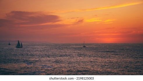 Dusk Beach Landscape With Three Sail Boats On The Background And Dusky Cloudy Sky Near The Coastline