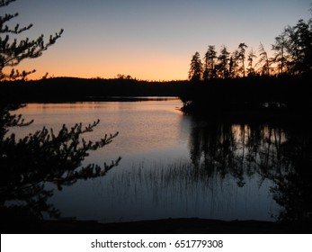 Dusk Settling Over A Calm Lake In The North Surrounded By The Dark Treeline Of A Coniferous Forest