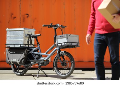 Dusseldorf / Germany – April 22, 2019: Cargo Ebike And Delivery Man With Boxes In Front Of An Orange Container On April 22, 2019 In Dusseldorf.