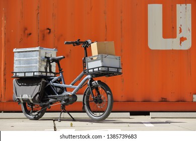 Dusseldorf / Germany – April 22, 2019: Cargo ebike with delivery boxes in front of an orange container on April 22, 2019 in Dusseldorf.