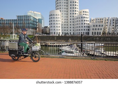 Dusseldorf / Germany – March 30, 2019: Cyclist With Cargo Ebike And Delivery Boxes Cycling Along Modern Media Harbor District On March 30, 2019 In Dusseldorf.