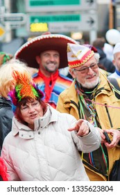 Dusseldorf, Germany - March 3rd 2019: Older Couple Of Seniors In Funny Carnival Hats Following The Festival Crowd In The Streets Of German Dusseldorf. The Woman Is Pointing With A Finger. 