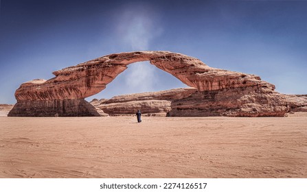 A "Dust Devil" or small tornado passes through "Rainbow Rock", also known as "Arch Rock' in Alula, Saudi Arabia. A man wearing traditional Clothes stands right under the arch.  - Powered by Shutterstock