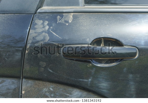 Dust on the black car. Car\
door handle. Scratches on the metal body of the car. Dusty metal\
surface.