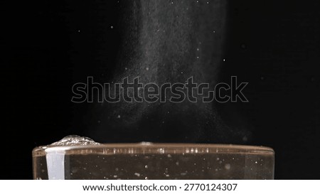 Dust particles cascade gracefully over a glass of water creating bubbles. Concept for freshness, mystery, and science-related topics.