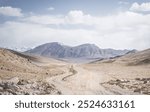 Dusty road of the Pamir Highway winds and twists in the valley of the Tien Shan mountains in Tajikistan in Pamir, landscape in the high desert mountains for background