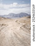 Dusty road of the Pamir Highway winds and twists in the valley of the Tien Shan mountains in Tajikistan in Pamir, landscape in the high desert mountains for background