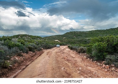 Dusty Road With Silver Car On Corsica Coast And Sea Clouds And Rainbow.