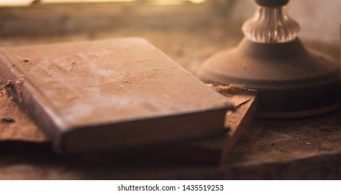 Dusty Window Sill In An Abandoned House. Lamp And Books In The Dust. Soft Warm Light Shines From The Window.