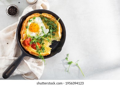 Dutch baby pancake with egg, greens and tomatoes in a cast-iron pan on a white table, top view, sunlight,  breakfast