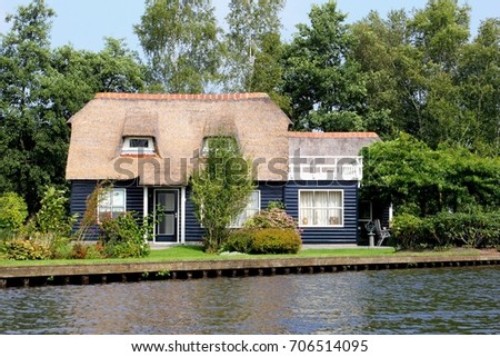 Dutch blue wooden house in traditional style, typical straw roof and charming garden terrace along water in scenic village Giethoorn, 'little Venice', Netherlands