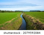 Dutch countryside landscape, Typical polder and water land, Green meadow on the blue sky. Small canal or ditch on the field, Friesland Netherlands