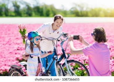 Dutch Family Riding Bicycle In Tulip Flower Fields In Netherlands. Mother And Kids Taking Selfie Picture With Mobile Phone Camera On Bikes At Blooming Tulips In Holland. Parents And Children Biking.