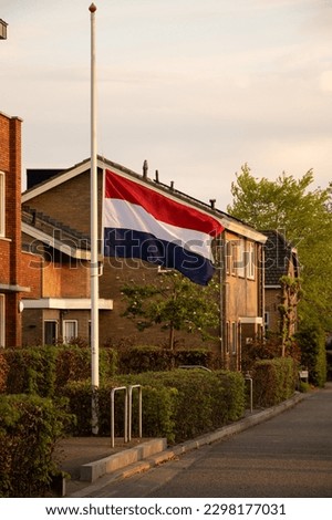 Dutch flag flies at half mast in residential street in Netherlands to pay respect to fallen soldier heroes. May 4th is National Remembrance Day or Dodenherdenking in Holland for commemoration 