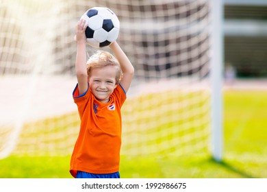 Dutch kids play football on outdoor field. Netherlands team fans with national flag. Go Holland! Children score goal at soccer game. Child in flag jersey kicking ball. Fan celebrating victory at pitch - Powered by Shutterstock