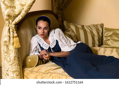 Dutch Master style portrait of a beautiful young woman in authentic renaissance costume lying on a luxury antique canopy bed in a golden bedroom of a medieval French castle with property release