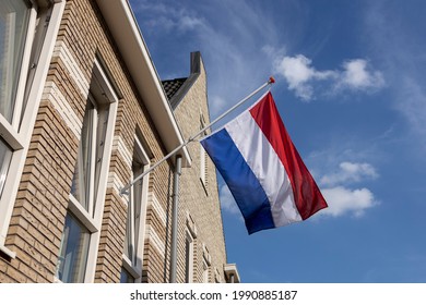 Dutch national flag hanging on the exterior facade of a modern building during the European soccer championship with vibrant blue sky and clouds in the background
