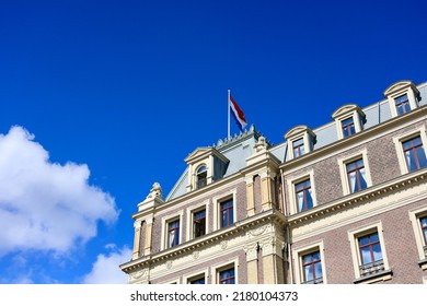 Dutch national flag hanging on the exterior facade of Amstel hotel with vibrant blue sky and clouds in the background. Amsterdam, The Netherlands. 