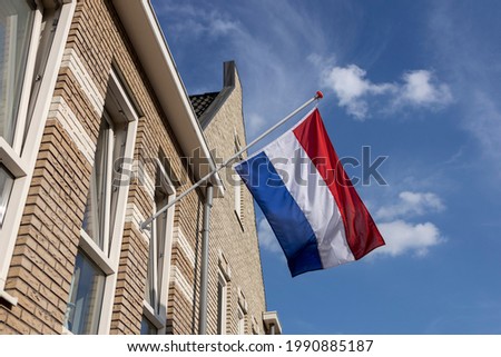 Dutch national flag hanging on the exterior facade of a modern building during the European soccer championship with vibrant blue sky and clouds in the background