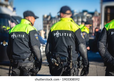 Dutch police squad formation and horseback riding mounted police back view with "Police" logo emblem on uniform maintain public order after football game and rally in the streets of Amsterdam center