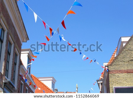 Dutch red white blue orange flags in blue sky between roof tops of old buildings, Fifa World Championship football in Qatar, Netherlands
